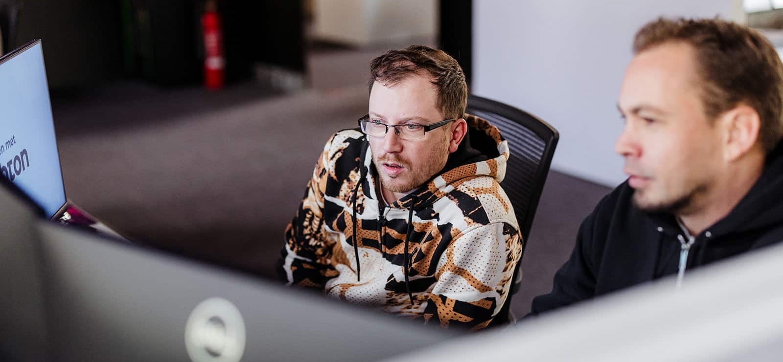 Twee collega’s bekijken geconcentreerd een computerscherm op kantoor tijdens een werksessie.