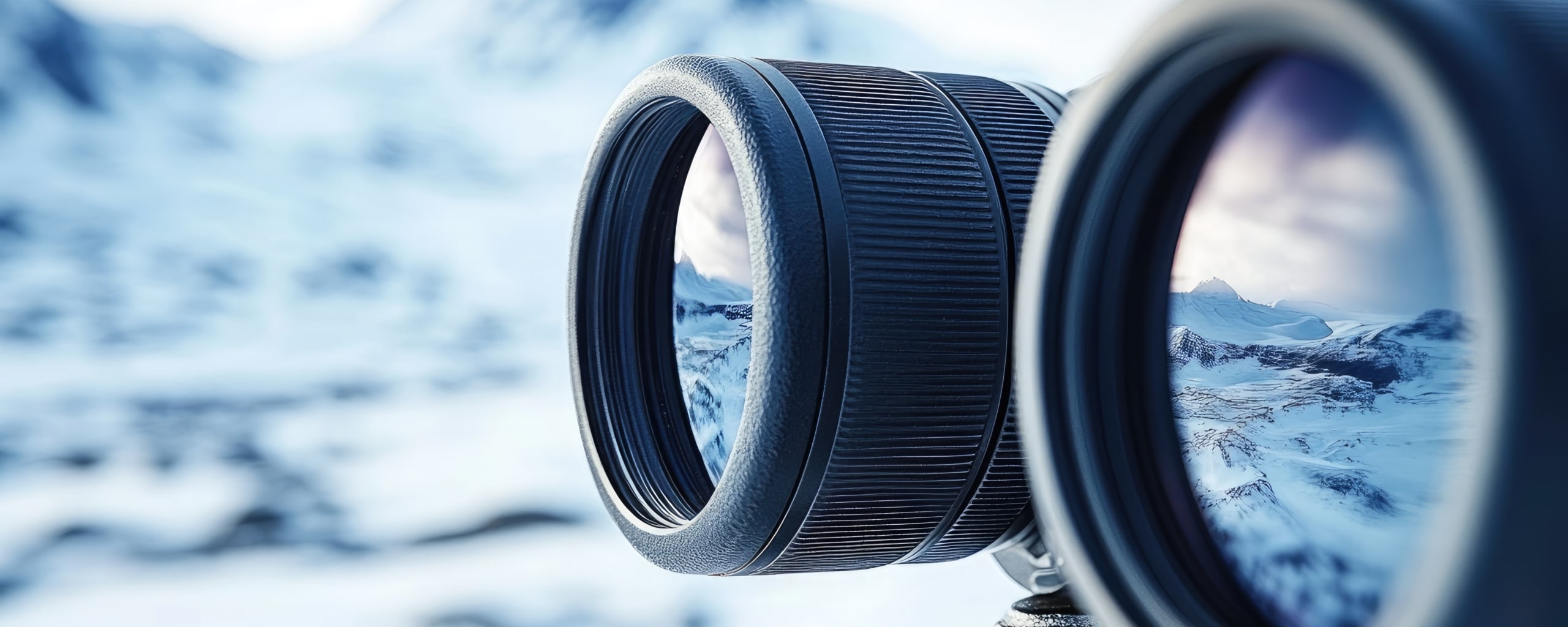 Close-up van twee cameralenzen met weerspiegeling van een berglandschap in de glazen elementen.
