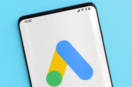 Smartphone met Google Ads-logo op het scherm tegen een lichtblauwe achtergrond.
