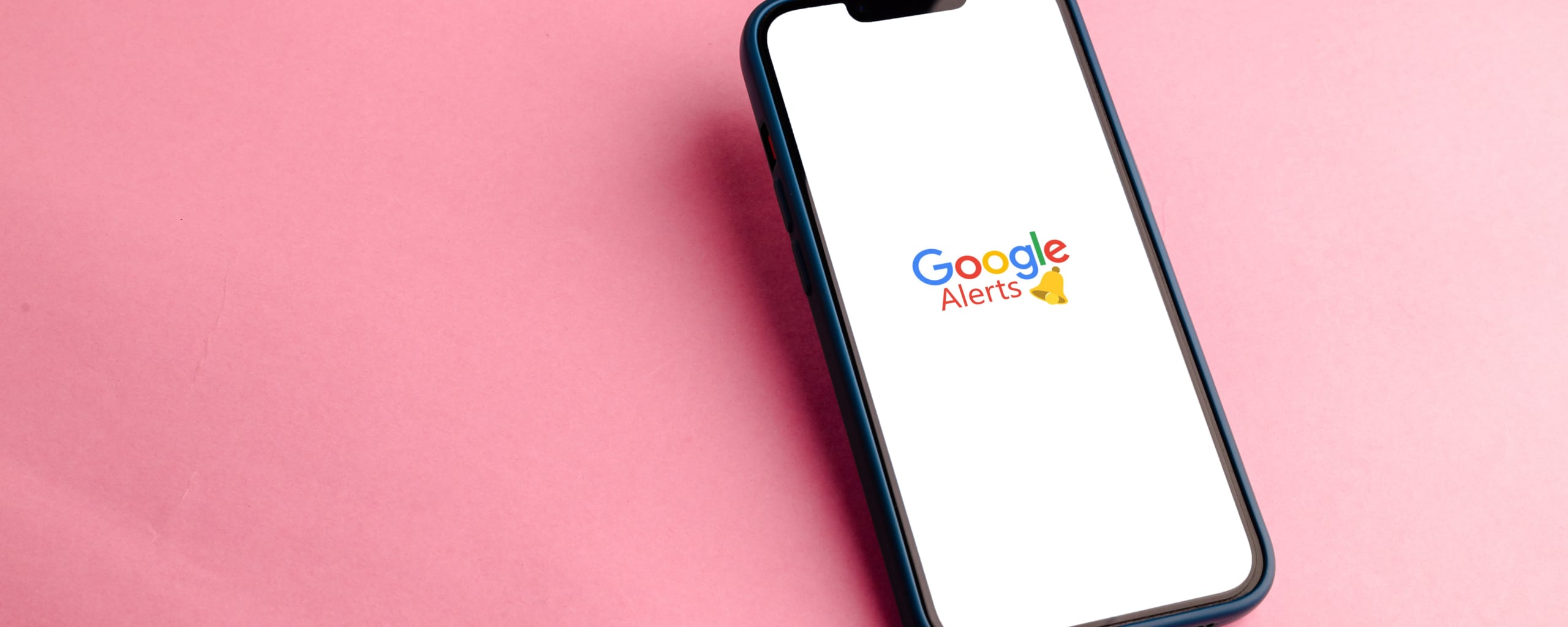 Smartphone met het Google Alerts-logo op het scherm tegen een roze achtergrond.