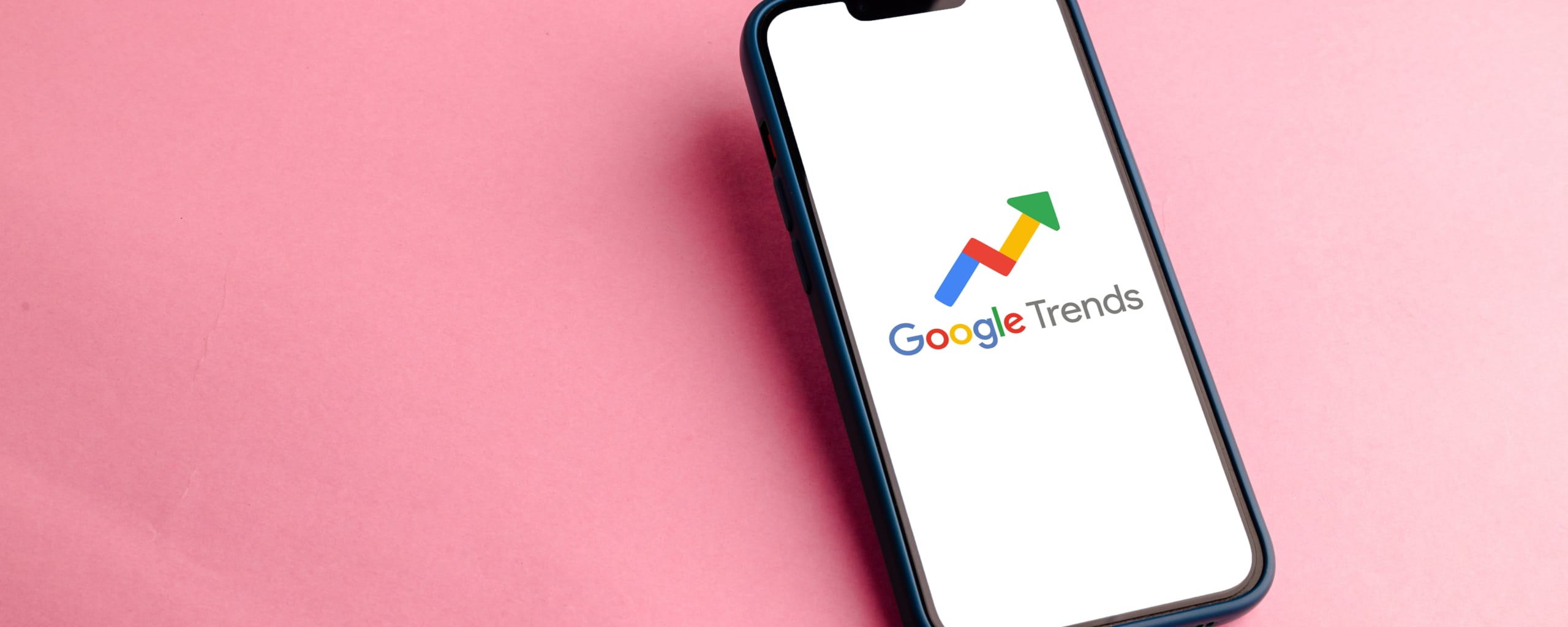 Smartphone op een roze achtergrond met het logo van Google Trends zichtbaar op het scherm.