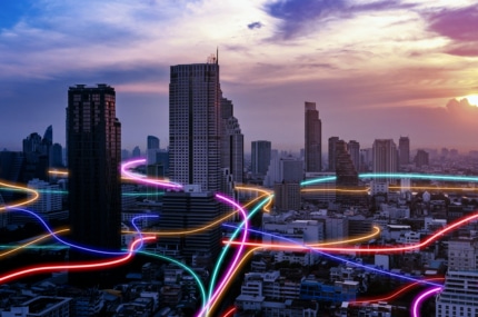 Stedelijke skyline bij zonsondergang met kleurrijke lichtlijnen die door de stad lopen en digitale connectiviteit symboliseren.