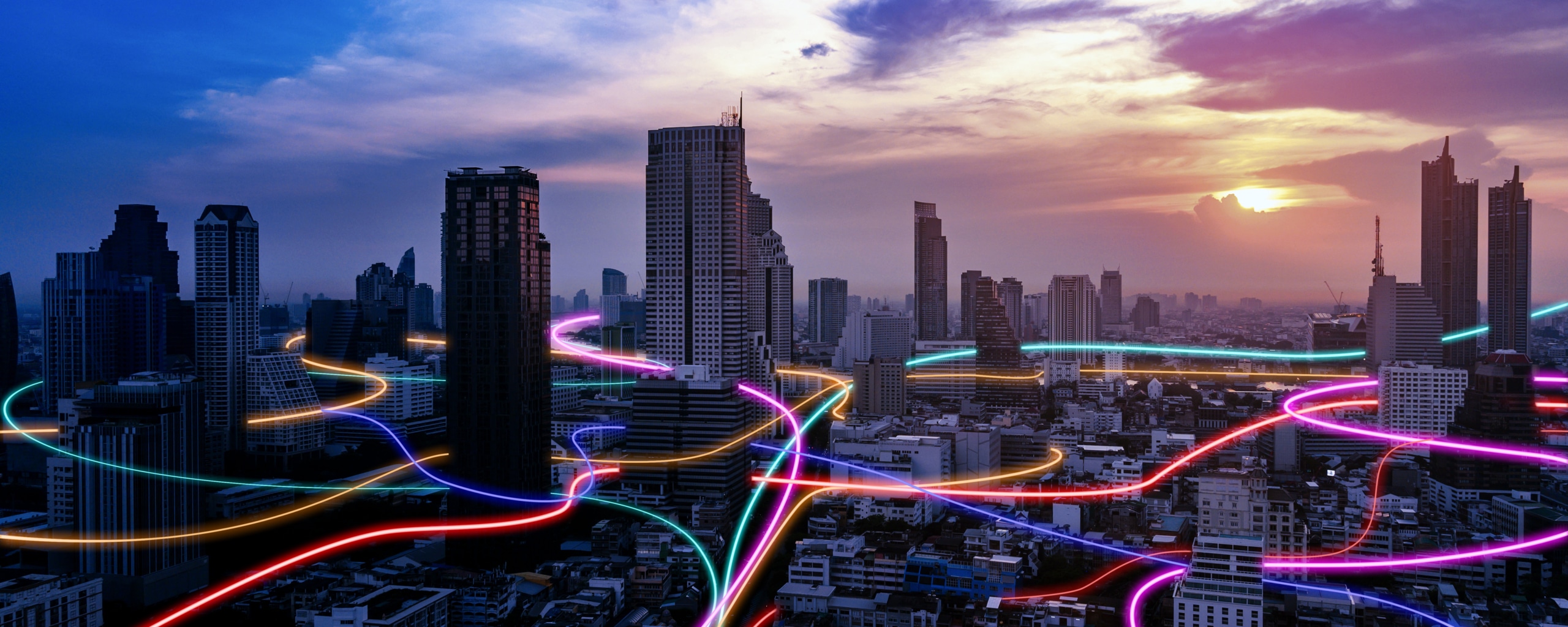 Stedelijke skyline bij zonsondergang met kleurrijke lichtlijnen die door de stad lopen en digitale connectiviteit symboliseren.