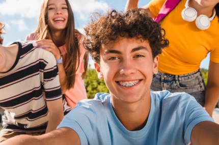 Groep lachende tieners die samen een selfie maken buiten op een zonnige dag.
