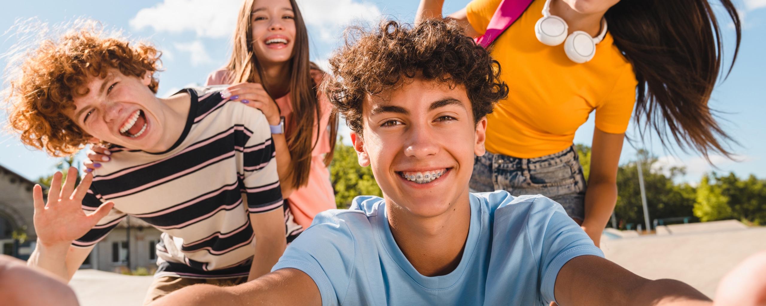 Groep lachende tieners die samen een selfie maken buiten op een zonnige dag.