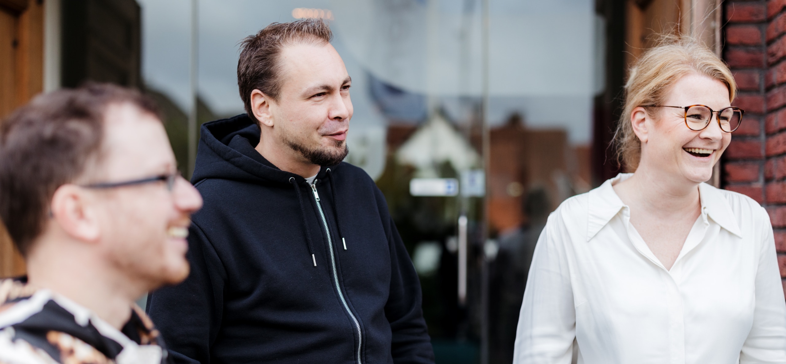 Drie collega’s staan buiten bij de ingang van een kantoor en lachen samen tijdens een gesprek.