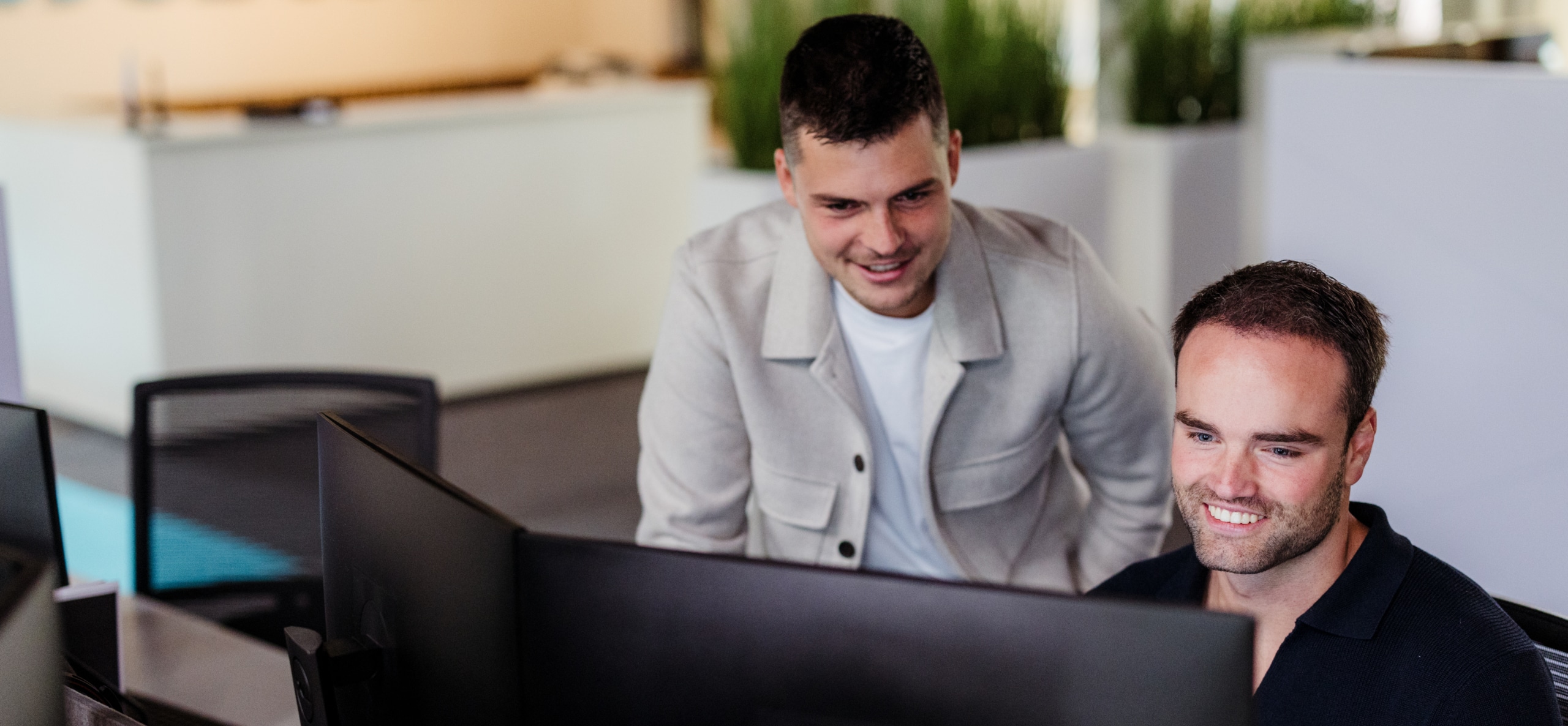 Twee collega’s werken samen achter een computerscherm en kijken geconcentreerd naar het beeld in een moderne kantoorruimte.