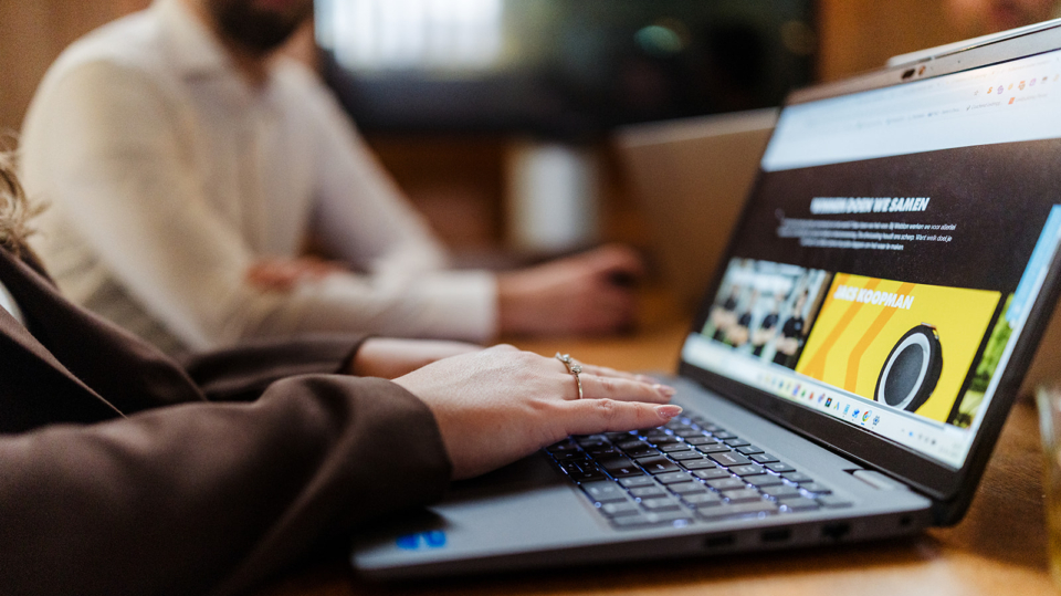 Close-up van iemand die werkt op een laptop met grafieken en data op het scherm tijdens een overleg.