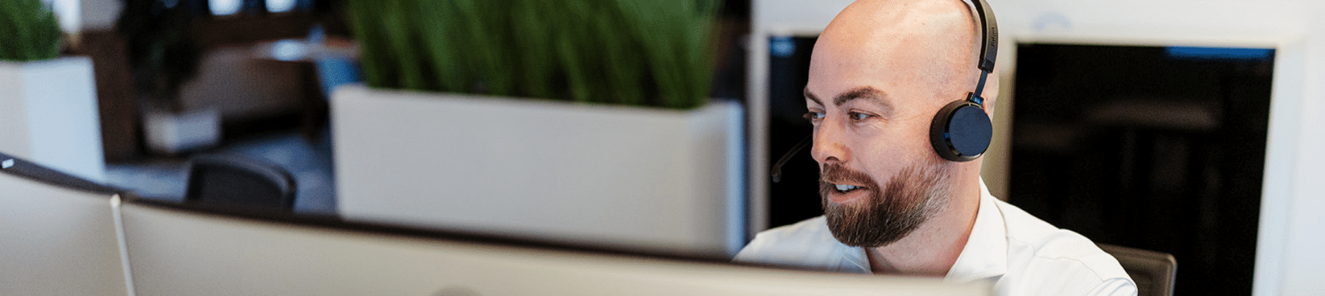 Een man met headset werkt achter zijn computer in een kantooromgeving, waarschijnlijk tijdens een online gesprek of klantcontact.