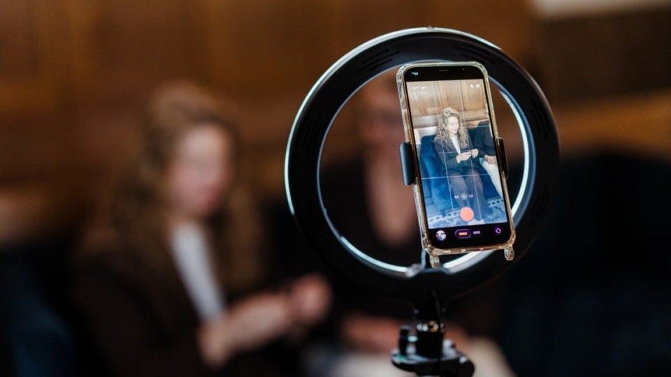 Een smartphone staat in een ringlamp en filmt een vrouw die een product presenteert voor een social media- of video-opname.