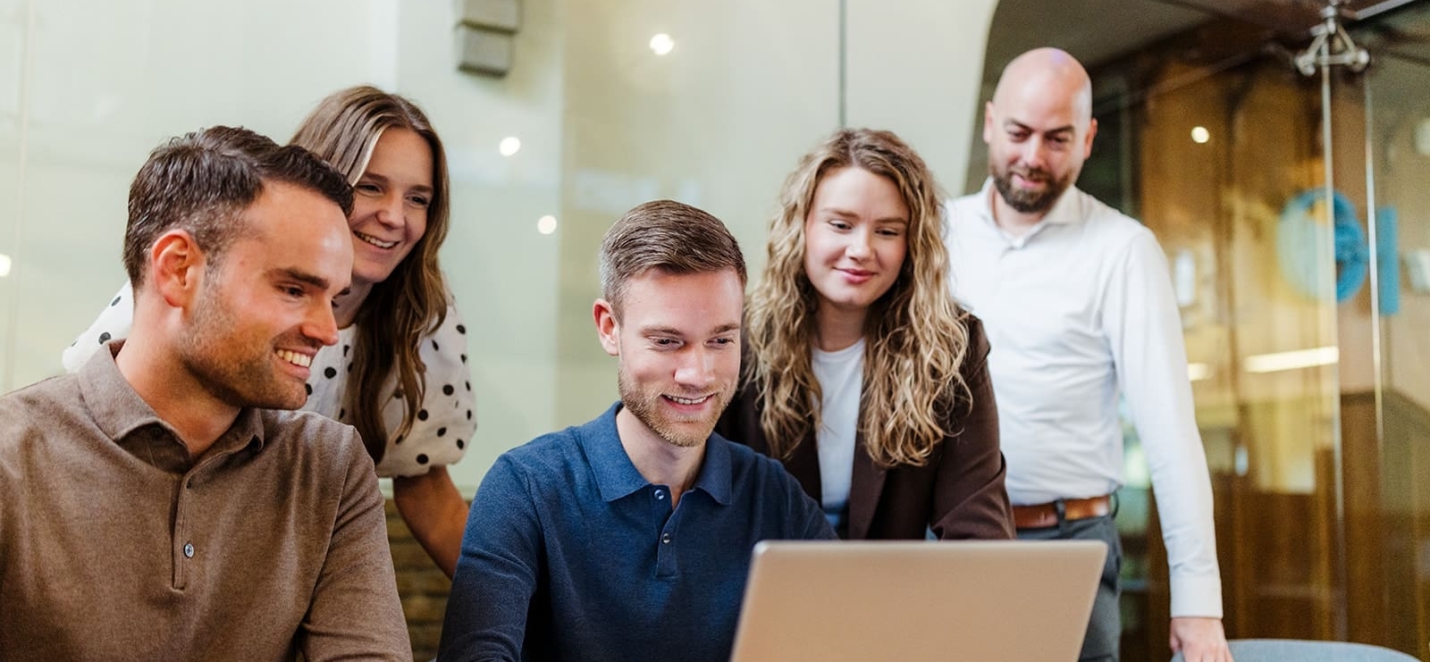 Een team van vijf mensen in een vergaderruimte kijkt naar een laptop. Ze zijn gefocust op de gegevens op het scherm, met een ontspannen en gemotiveerde sfeer.