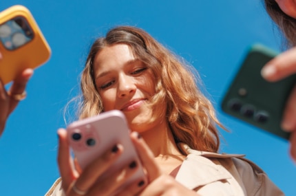 Drie jongeren kijken op hun smartphones tegen een heldere blauwe lucht op de achtergrond.