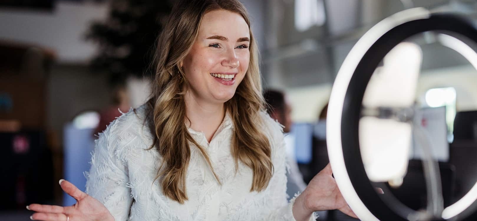 Een vrouw spreekt glimlachend in een smartphonecamera met ringlamp, alsof ze een video opneemt voor social media of online content.