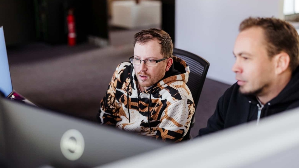 Twee collega’s zitten naast elkaar achter een computer en kijken geconcentreerd naar het scherm tijdens het werk.