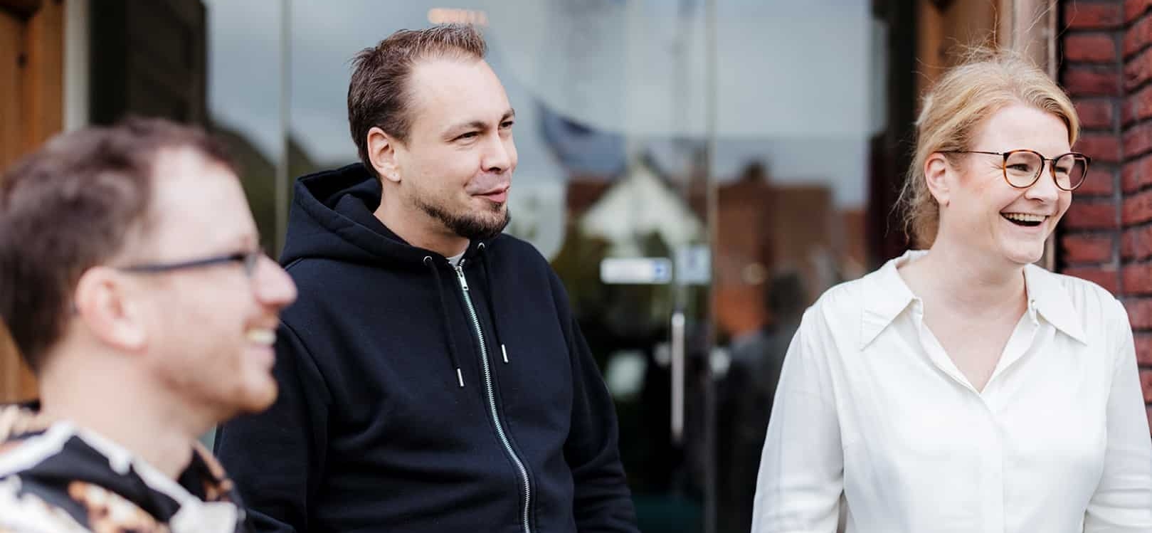 Drie collega’s staan buiten bij de ingang van een kantoor en lachen samen tijdens een gesprek.