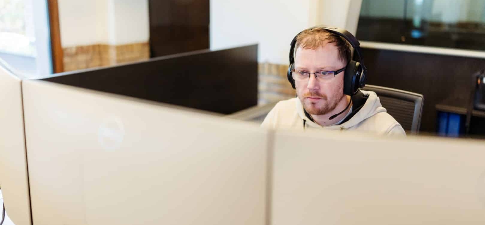 Een medewerker met headset werkt geconcentreerd achter meerdere computerschermen in een kantooromgeving.