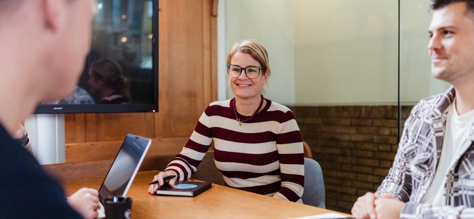 Drie collega’s zitten aan een vergadertafel tijdens een overleg in een kantoorruimte.