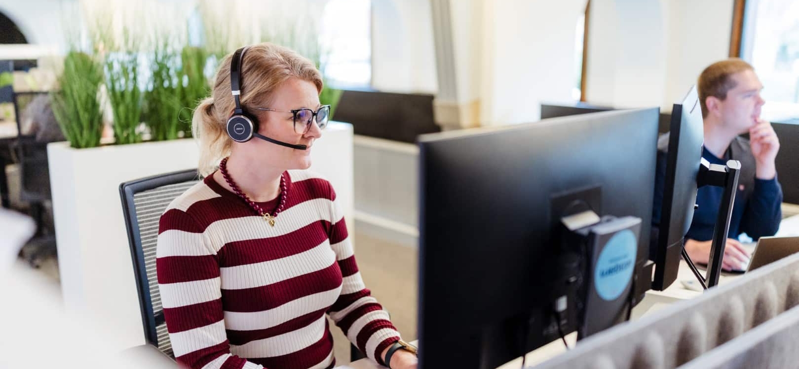 Een medewerker met headset werkt achter een computerscherm in een moderne kantooromgeving.