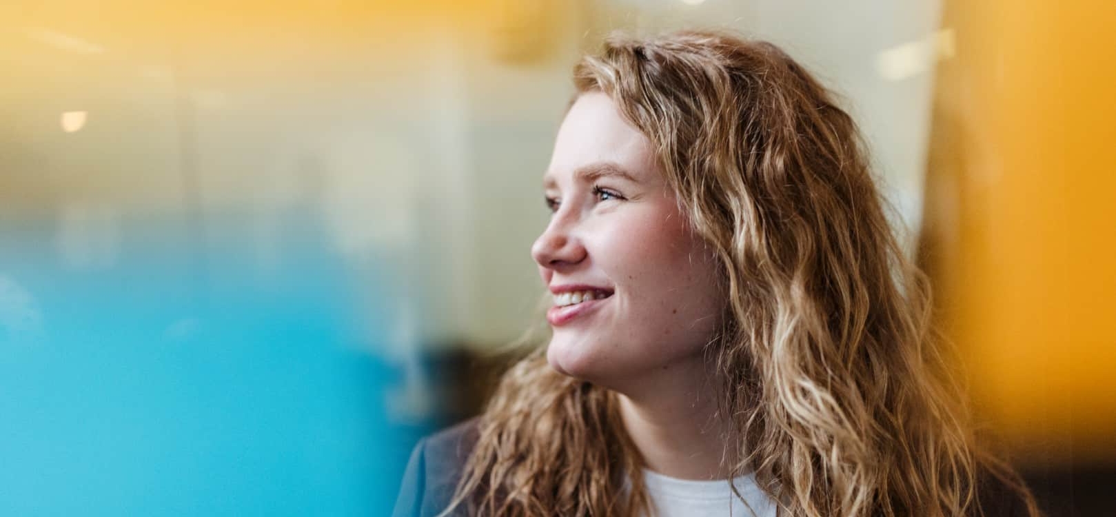 Een vrouw met krullend haar kijkt lachend opzij in een kantooromgeving.