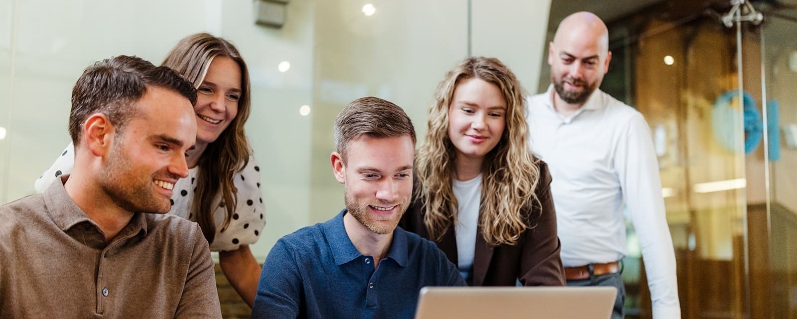 Een team van vijf mensen in een vergaderruimte kijkt naar een laptop. Ze zijn gefocust op de gegevens op het scherm, met een ontspannen en gemotiveerde sfeer.
