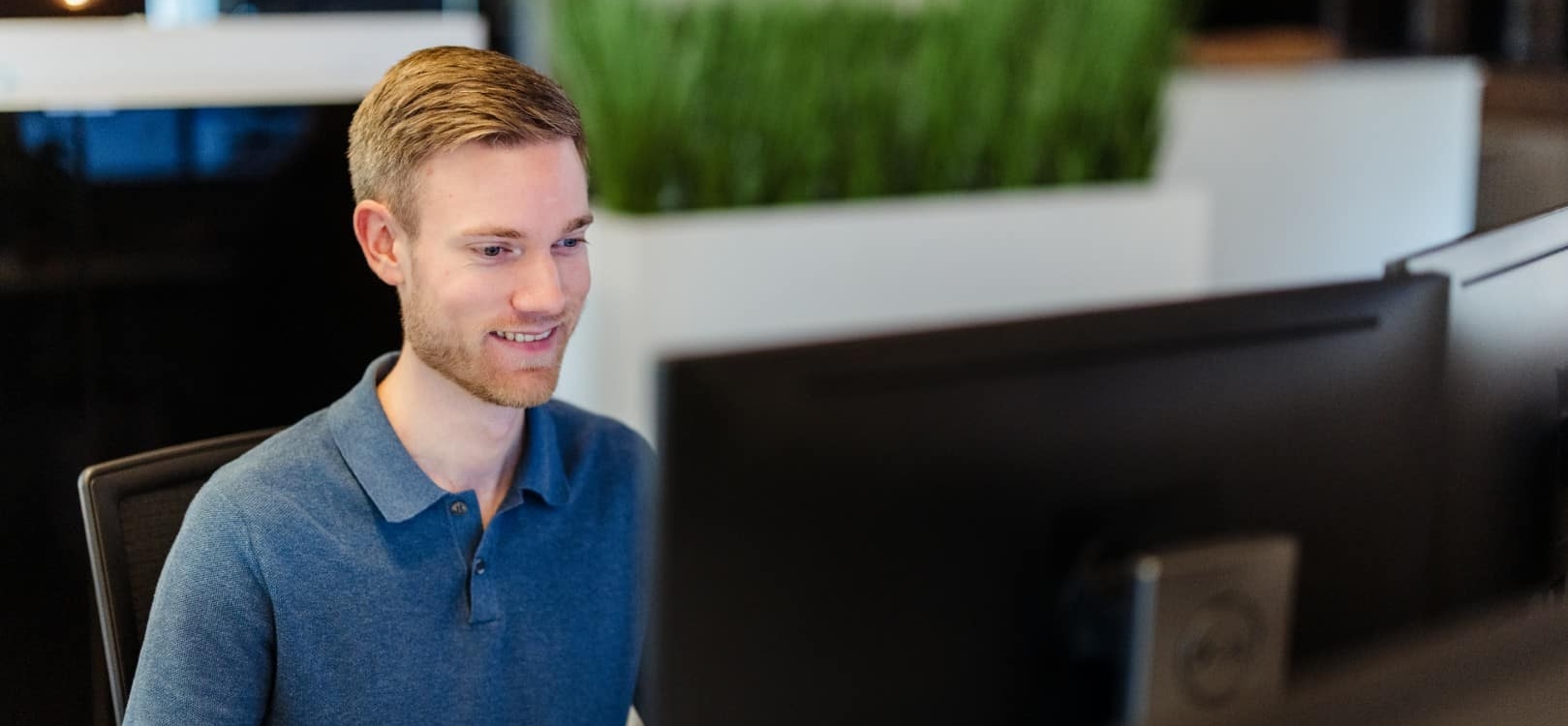 Een medewerker werkt geconcentreerd achter een computerscherm in een moderne kantooromgeving.