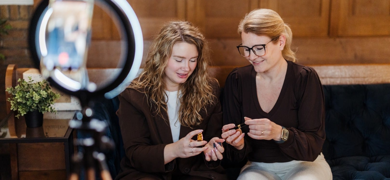 Twee vrouwen zitten samen op een bank en bekijken een product terwijl ze worden gefilmd met een smartphone in een ringlamp