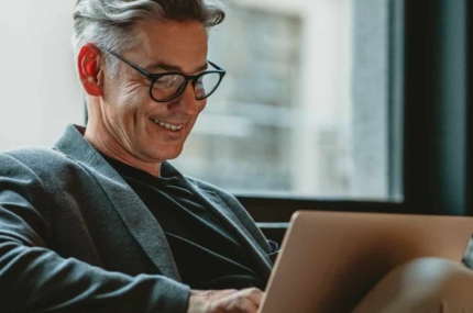 Man met bril werkt ontspannen op een laptop in een moderne kantooromgeving.